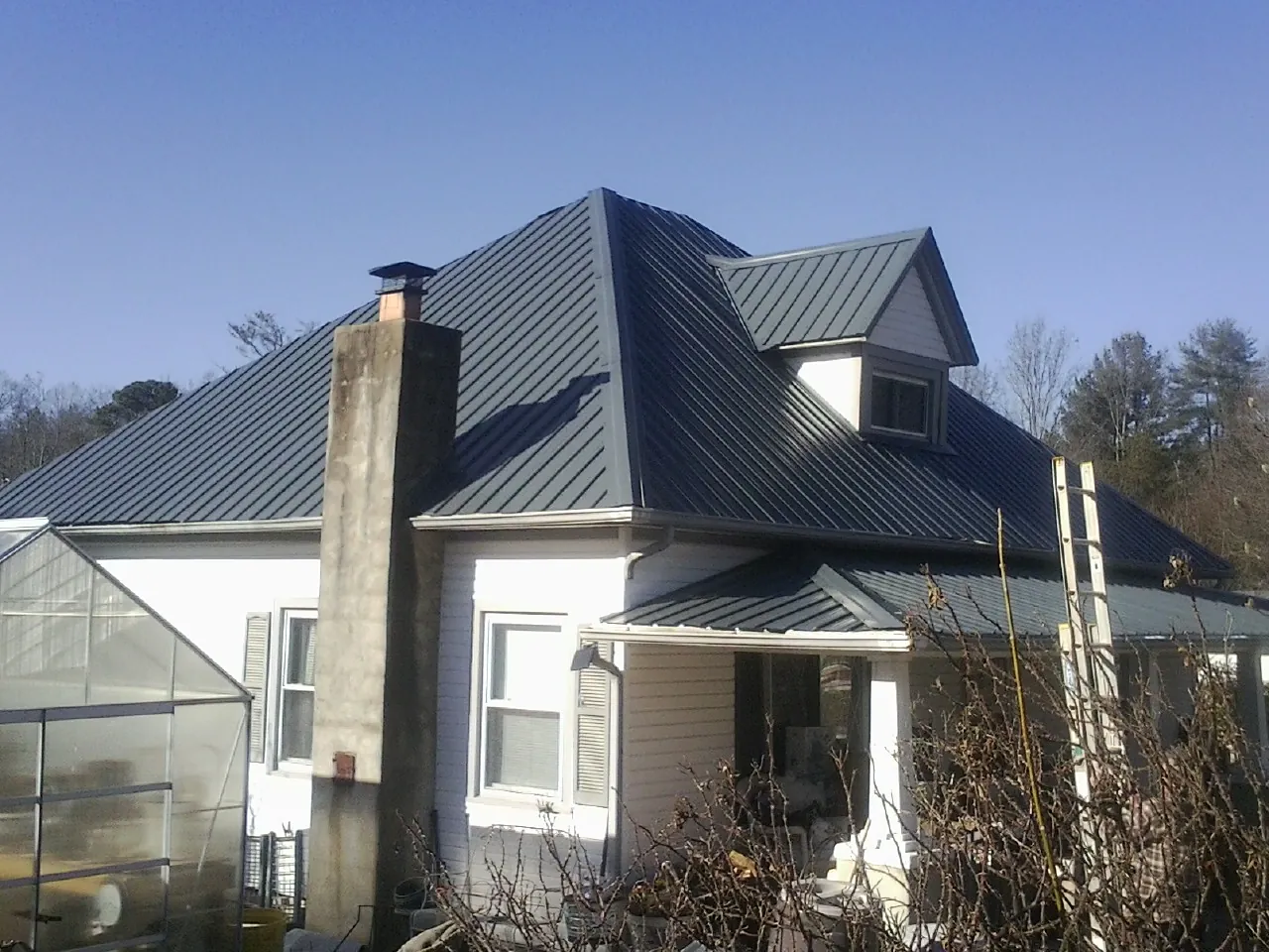 Dark blue standing seam metal roof on a white farmhouse with dormer — Slate & Tile Roof Repair by Roofing Brothers in Algonac