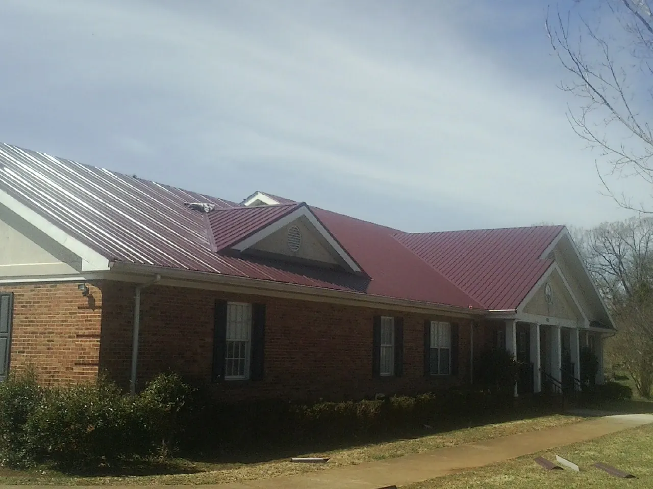 Red metal roof with gabled entries on a long brick building, from a Hail Damage Roof Repair job in Algonac