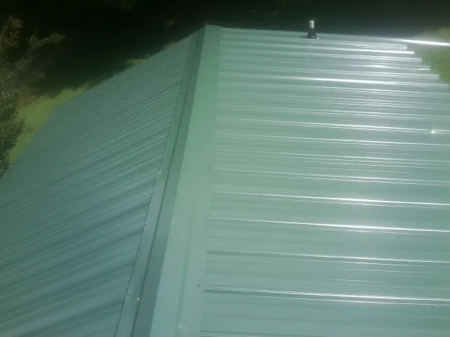 New green metal panels meeting at the ridge of a roof — Flat Roof Repair work by our crew in Algonac