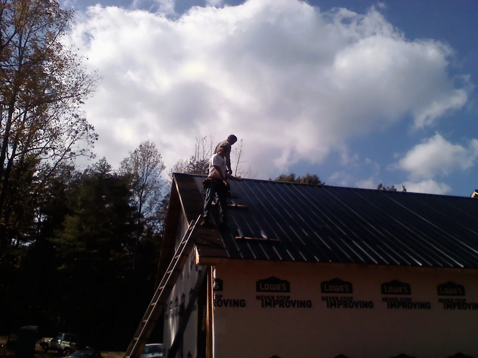Roofer fastening dark metal panels high against a cloudy sky, from a Roof Inspection job in Algonac